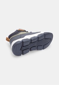 Sneaker per bambino di colore blu scuro e oliva con suola nera texturizzata e linguetta arancione, mostrato dal basso e da un'angolazione laterale.