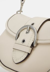 Cream-colored leather handbag with a rounded flap, silver hardware, and contrasting dark stitching. Features a decorative buckle closure.