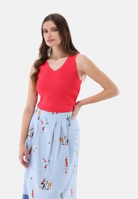 Rotes, geripptes Strick-Top mit V-Ausschnitt, kombiniert mit einem hellblauen Rock, der farbenfrohe Modeillustrationen und Falten aufweist.