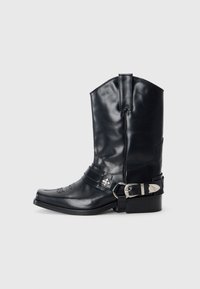Bota de vaquero de cuero negro con punta afilada, caña alta, costuras decorativas y herrajes de hebilla plateada en la correa. Acabado texturizado.