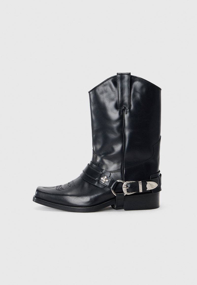 Bota de vaquero de cuero negro con punta afilada, caña alta, costuras decorativas y herrajes de hebilla plateada en la correa. Acabado texturizado.