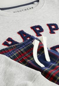 Jasnoszara bluza z kapturem z napisem "HAPPY" w granatowej i czerwonej, puszystej haftowanej aplikacji, zestawiona z granatowymi spodniami w kratę z czerwonymi i zielonymi akcentami oraz białymi sznurkami.