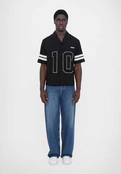 Black short-sleeve button-up shirt with white stripes and number "10" on the front, paired with light blue wide-leg jeans and white sneakers.