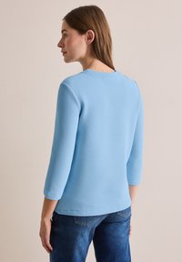 Lichtblauw, gestructureerd shirt met lange mouwen en een ronde halslijn, gecombineerd met donkerblauwe spijkerbroek.