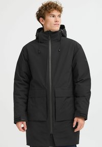 Črna parka jakna z sprednjim zadrgo, nastavljivo kapuco in dvema velikima sprednjima žepoma. Gladka tekstura, s slim fit krojem in minimalnim dizajnom.