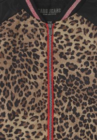 Leopardikuvioinen takki, jossa on punaisella reunustettu vetoketju, mustat olkapäät ja ribbineulekaulus, jossa on punaisia ja valkoisia raitoja.