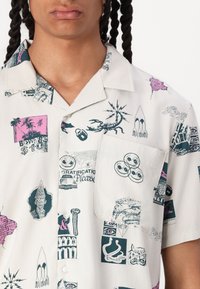 Short-sleeve, button-up shirt in white with colorful graphic prints, including scorpions, symbols, and text. Features a chest pocket.