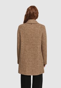 Abrigo marrón de pata de gallo con cuello y mangas largas, que presenta un tejido texturizado y una forma ligeramente entallada, que llega por debajo de las caderas.