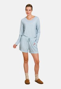 Lichtblauw, lange mouwen top met een ronde halslijn en gestructureerd patroon; gecombineerd met bijpassende shorts en bruine slippers.