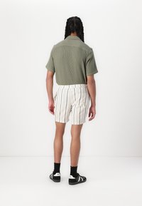 Chemise à manches courtes, vert olive texturé, associée à un short à taille élastique rayé crème et des baskets noires, vue de dos.