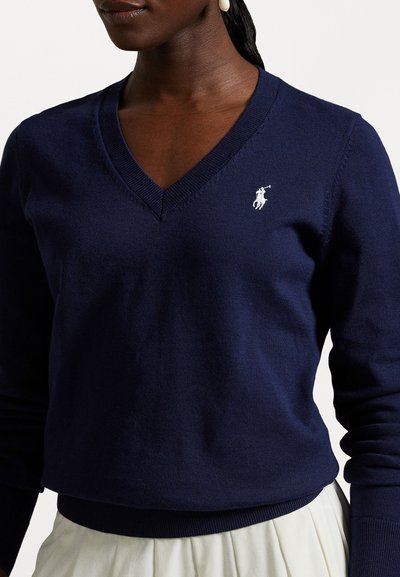 Sötétkék V nyakú pulóver, puha kötött anyagból készült, fehér logóval a bal mellen és bordás mandzsettákkal, valamint szegélyezéssel.