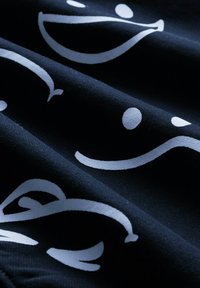 Un tissu noir présente des motifs graphiques blancs, notamment des visages souriants et des points, avec une surface texturée créant un contraste visuel.