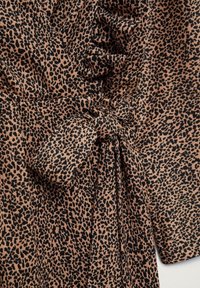 Tissu imprimé léopard avec un détail de nœud noué et une couture froncée sur un vêtement, présentant de petites taches noires sur un fond beige.