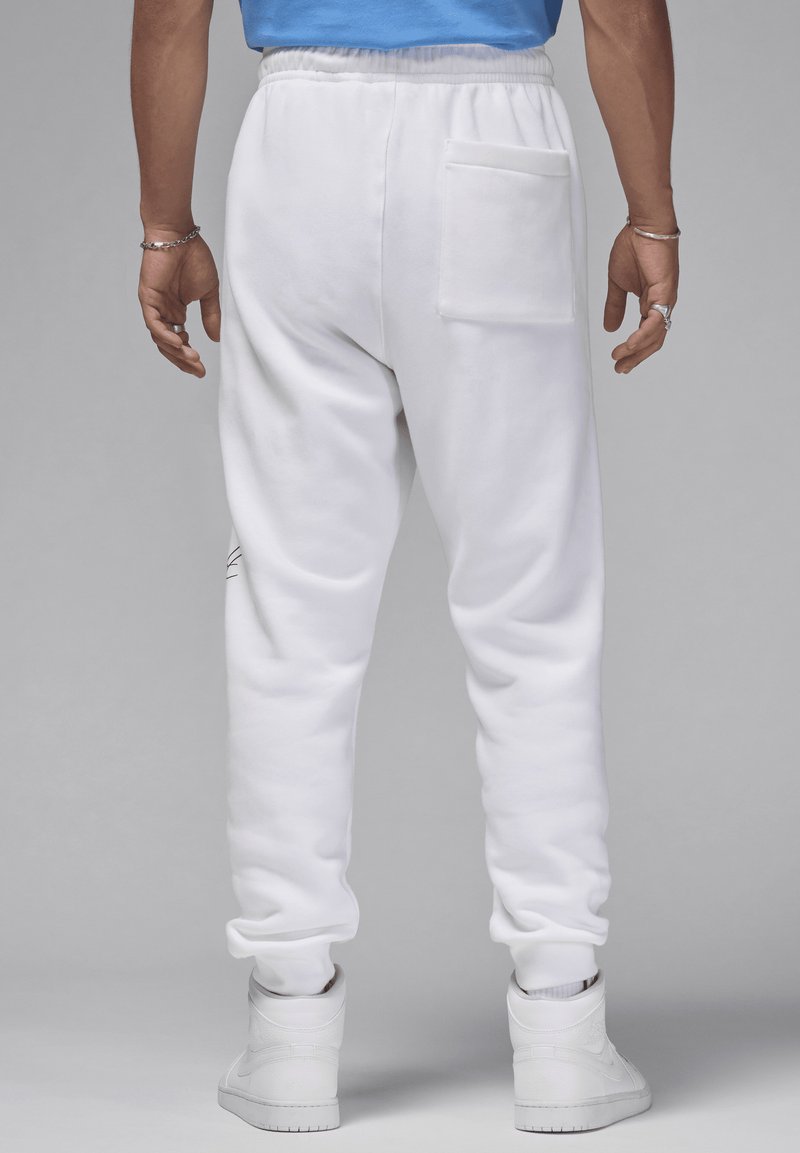 Weiße Sweatpants aus weichem Material mit schmal zulaufendem Schnitt, ausgestattet mit einer Gesäßtasche und dezenten seitlichen Designelementen. Kombiniert mit weißen Sneakern.