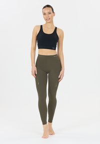 Svart sport-bh och olivgröna leggings, med en mjuk textur, hög midja och dekorativa utskärningar längs sidorna.