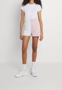 Šortky s bílými a růžovými bloky barev s elastickým pasem, doplněné o přiléhavé bílé tričko a bílé tenisky. Hladká, neformální látka.