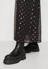 Svarta läderankelstövlar med en tjock, strukturerad sula, med en slip-on design. Överdraget med genomskinlig svart tyg med metalliska prickar.