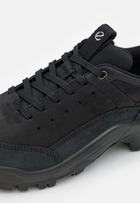 Chaussure de sport noire avec dessus en suède et mesh, lacets ronds, détails perforés et semelle en caoutchouc texturée avec crampons antidérapants.