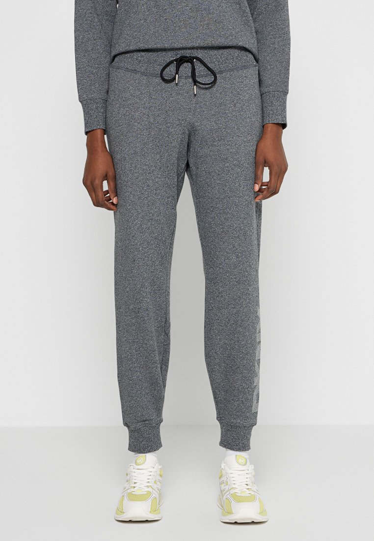 Szare dresy wykonane z teksturowanej tkaniny, z elastyczną talią, regulowanym sznurkiem oraz zwężanymi mankietami, połączone z białymi i żółtymi trampkami.