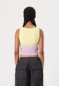 Ribbed crop tank top with a gradient from yellow to lavender, featuring a round neckline and wide shoulder straps, worn with dark cargo pants.
