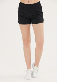 Zwarte sportshorts van lichtgewicht stof met een elastische tailleband en zijsplitten voor bewegingsvrijheid, gecombineerd met witte sneakers.