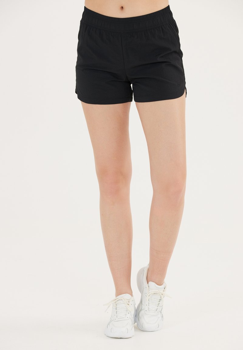 Zwarte sportshorts van lichtgewicht stof met een elastische tailleband en zijsplitten voor bewegingsvrijheid, gecombineerd met witte sneakers.