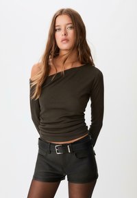 Mørke olivengrøn langærmet top med off-shoulder design og ribbet tekstur, parret med sorte højtaljede shorts med bælte.