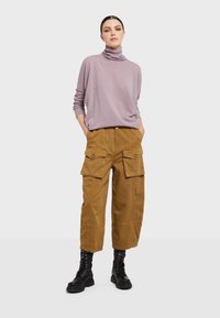 Jasnofioletowy sweter z golfem, luźny krój, zestawiony z beżowymi spodniami cargo z dużymi przednimi kieszeniami, noszony z czarnymi lace-up botkami wojskowymi.