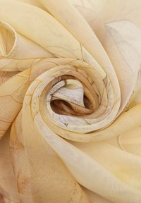 Sciarpa gialla a motivi, realizzata in tessuto leggero, presenta una consistenza morbida e traslucida con disegni vorticosi e toni terrosi sottili.