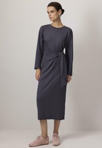 Vestido midi gris oscuro con mangas largas y detalle de cintura anudada, combinado con zapatillas rosa claro. Tejido suave y elástico.