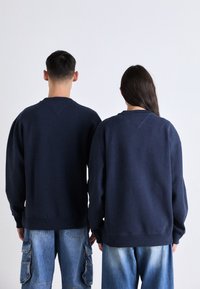 Námornícky modré oversized mikiny s okrúhlym výstrihom, s rebrovanými manžetami a lemami, nosené dvoma jednotlivcami. Neformálny štýl s uvoľneným strihom.