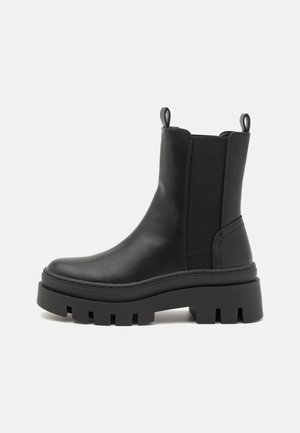 Botas chelsea de couro preto com painéis laterais elásticos, alças de puxar e uma sola de borracha espessa e robusta com detalhes recortados.