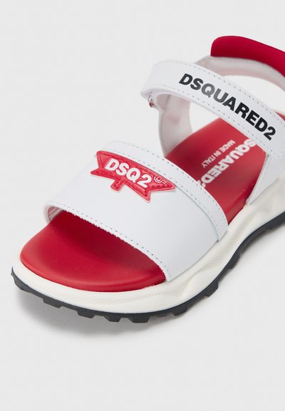 Sandale blanche avec accents rouges et logo, dotée de deux brides réglables, d'une semelle intérieure rembourrée et d'une semelle extérieure en caoutchouc noir texturée.