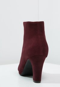 Bordeauxfarvet ruskindsankelstøvle med spids hæl, glat tekstur og slank silhuet. Har en rundet tå og minimalistisk detaljering.