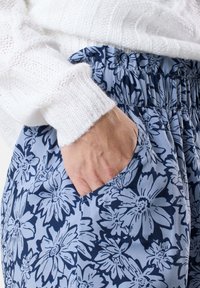 Blommig byxa med ljusblå bas, prydd med mörknavy blommönster, elastisk midja och sidoficka. Texturerad vit tröja synlig.