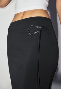 Black stretch skirt with a smooth texture, featuring a silver metal hardware accent and adjustable tie detail on the side.