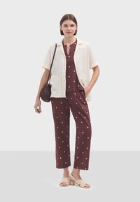 Chemise en lin à manches courtes de couleur crème ; haut et pantalon bordeaux avec des motifs en losange ; sandales beiges à lanières ; sac à main tressé marron.