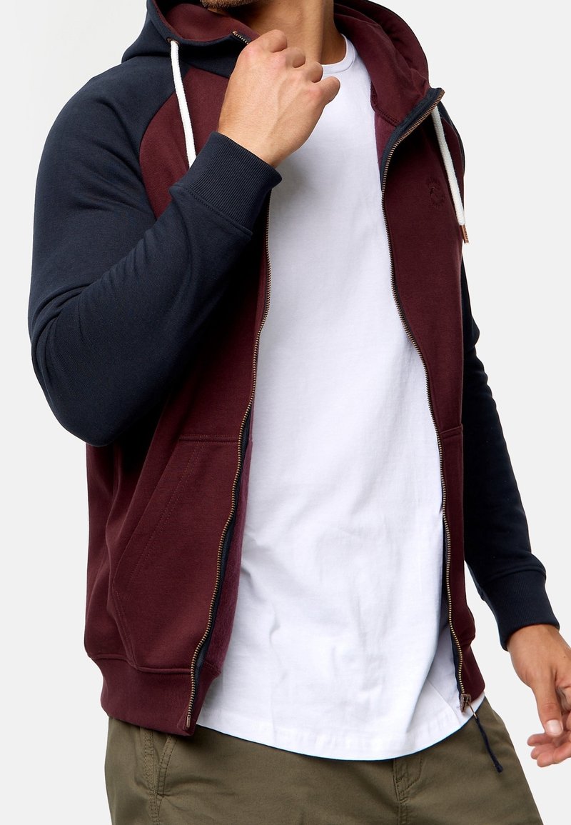 Rits hoodie in bordeaux en marineblauw, met een contrasterend ontwerp, zachte stof en een verstelbare trekkoordkap. Voorzakken inbegrepen.
