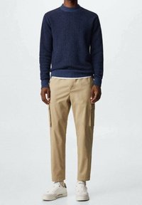 Maglione a costine di colore blu navy abbinato a pantaloni cargo khaki con tasche laterali, completato da sneakers bianche.