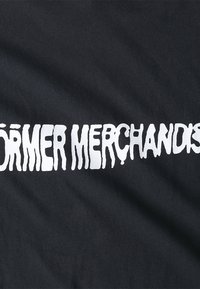 Black t-shirt with white, distorted text reading "FORMER MERCHANDISE." Fabric appears soft with a smooth texture and slight sheen.
