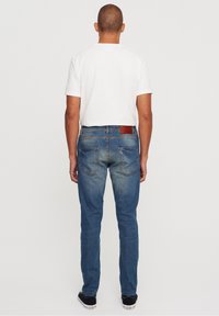 Blå denimjeans med rak passform, med en brun läderlapp och två bakfickor, kombinerade med en vit t-shirt och svarta sneakers.