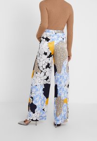 Wijduitlopende broeken met een mix van bloemen- en geometrische patronen in blauw, geel, zwart en wit. Lichtgewicht stof met een gladde textuur.