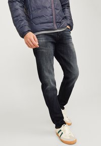 Tummansiniset farkut slim fit -mallia, joissa on hienovarainen rakenne ja ompeluyksityiskohdat, yhdistettynä kermaisiin urheilukenkiin ja toppatakkiin.