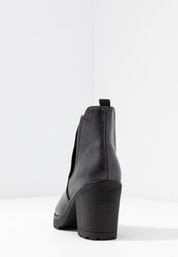 Černá kožená kotníková bota s kulatou špičkou, vysokým blokovým podpatkem, elastickými bočními panely a tahacím poutkem. Hladký povrch s viditelnými stehovými detaily.