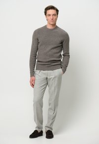 Maglione grigio lavorato a maglia, pantaloni grigio chiaro, scarpe scure. Il maglione ha un collo rotondo e polsini a costine, i pantaloni presentano una vestibilità sartoriale.
