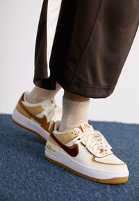 Baskets Nike Air Force 1 dans des tons crème et caramel ; dotées d'une surface texturée, de lacets légers et d'une semelle en caoutchouc avec une adhérence prononcée.