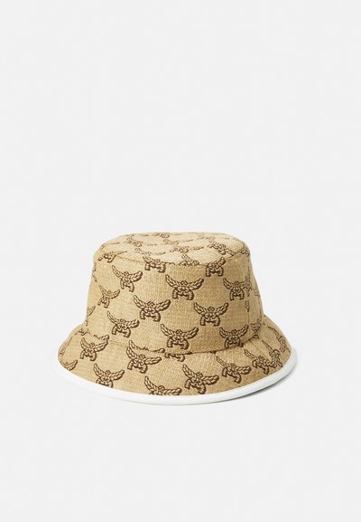 Beige bucket hat featuring a repeating brown winged design. Made of textured fabric with a contrasting white rim.