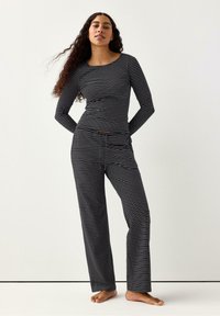 Svartvitrandig långärmad topp och matchande byxor. Tyget verkar mjukt med en figursydd design och en avslappnad byxsilhuett.