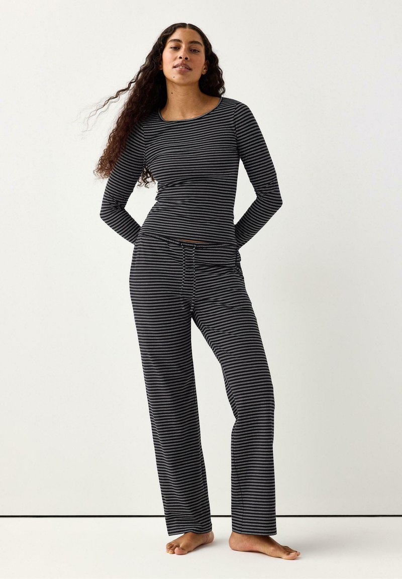 Svartvitrandig långärmad topp och matchande byxor. Tyget verkar mjukt med en figursydd design och en avslappnad byxsilhuett.