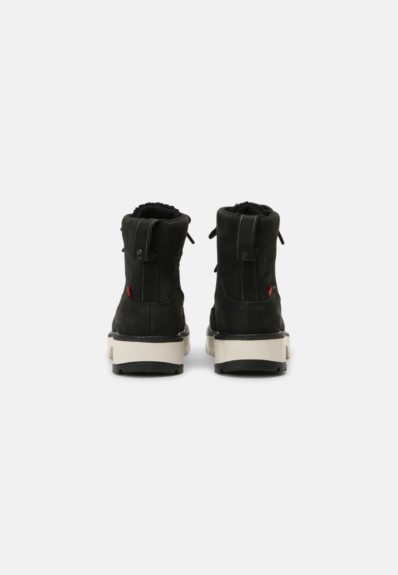 Botines de ante negro con suela de goma blanca, que presentan una parte superior texturizada, paneles laterales elásticos y un tirador en la parte trasera.